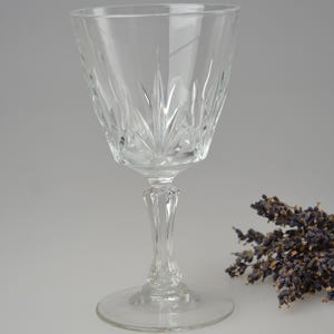 May include: A clear glass wine glass with a cut crystal design. The glass has a tall stem and a wide base. The glass is empty and is sitting on a white surface.