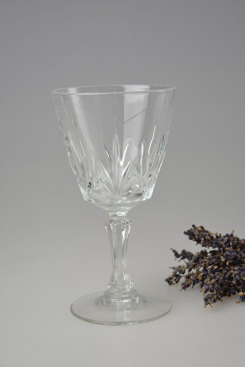 May include: A clear glass wine glass with a cut crystal design. The glass has a tall stem and a wide base. The glass is empty and is sitting on a white surface.