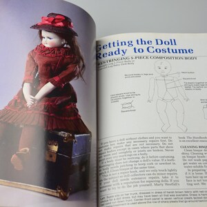 Pode incluir: Uma boneca vintage com um vestido vermelho e um chap&eacute;u de palha est&aacute; sentada em um ba&uacute; de madeira. A p&aacute;gina do livro mostra instru&ccedil;&otilde;es para re-encordoar um corpo de boneca de composi&ccedil;&atilde;o de 5 pe&ccedil;as. O texto diz "Getting the Doll Ready to Costume" e "Stringing 5-Piece Composition Body".
