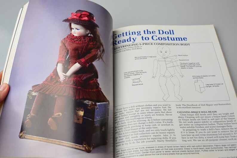 Pode incluir: Uma boneca vintage com um vestido vermelho e um chap&eacute;u de palha est&aacute; sentada em um ba&uacute; de madeira. A p&aacute;gina do livro mostra instru&ccedil;&otilde;es para re-encordoar um corpo de boneca de composi&ccedil;&atilde;o de 5 pe&ccedil;as. O texto diz "Getting the Doll Ready to Costume" e "Stringing 5-Piece Composition Body".