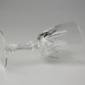 May include: A clear crystal wine glass with a round base, a detailed stem, and a bowl with a cut-glass design. The glass is lying on its side, showcasing its elegant shape and intricate patterns. Perfect for serving wine.