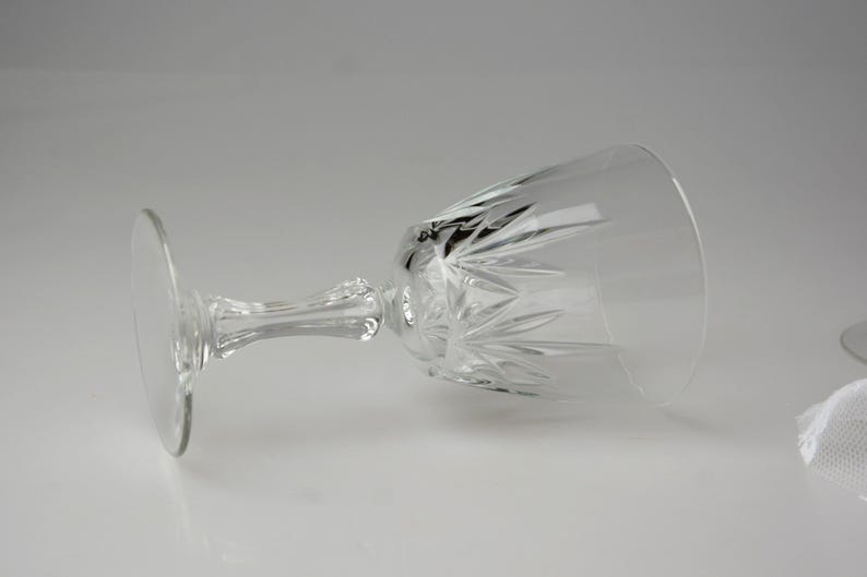 May include: A clear crystal wine glass with a round base, a detailed stem, and a bowl with a cut-glass design. The glass is lying on its side, showcasing its elegant shape and intricate patterns. Perfect for serving wine.