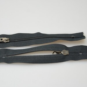 May include: Two black zipper pulls with silver metal sliders. The zippers are open and the slider is in the middle of the zipper.