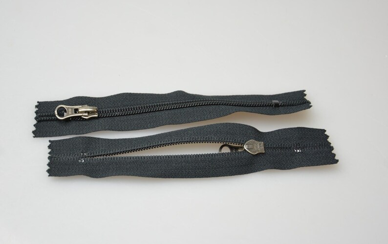 May include: Two black zipper pulls with silver metal sliders. The zippers are open and the slider is in the middle of the zipper.