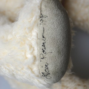 May include: Close-up of a white teddy bear's foot with a black signature that reads "Mona Rocner - 1987".