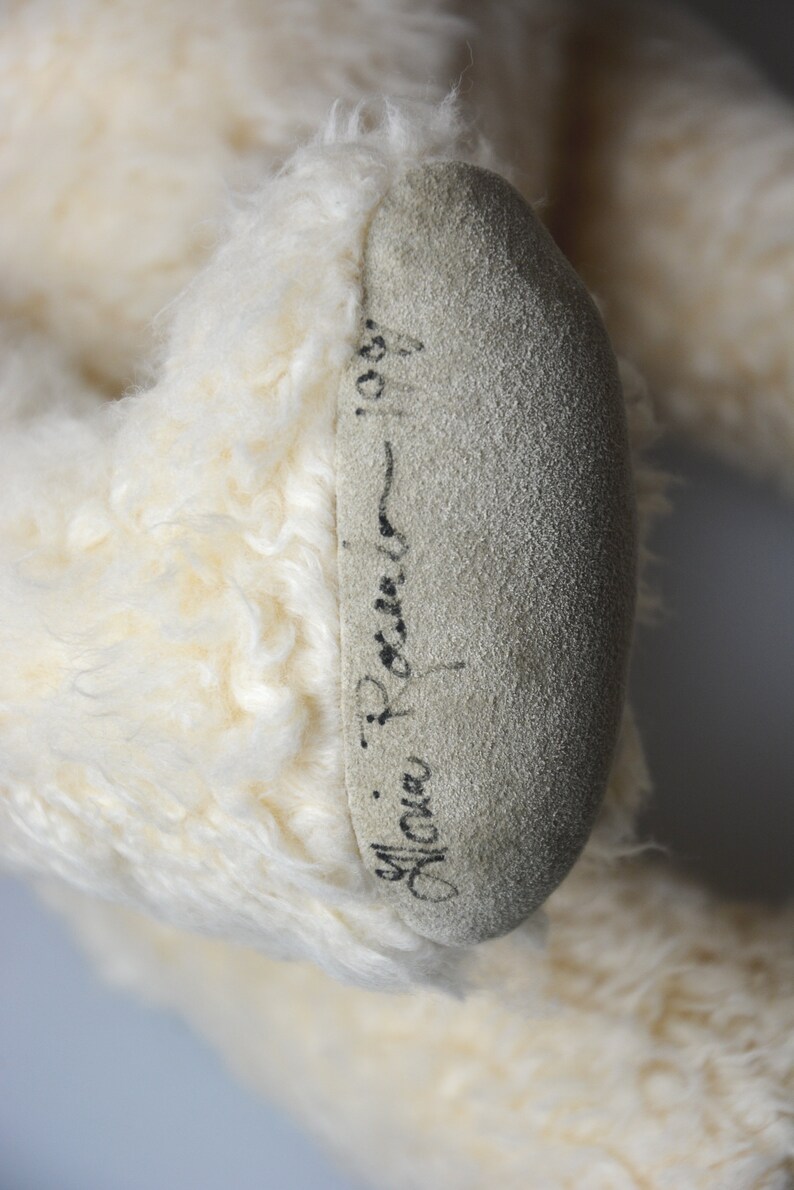 May include: Close-up of a white teddy bear's foot with a black signature that reads "Mona Rocner - 1987".