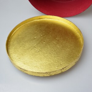 May include: A round, gold-colored lid for a box. The lid is made of cardboard and has a smooth, shiny surface.