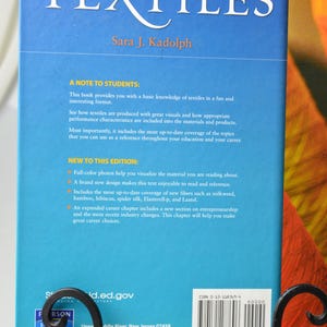 Puede incluir: La contraportada de un libro azul titulado "TEXTILES" de Sara J. Kadolph. El libro es la d&eacute;cima edici&oacute;n e incluye fotos a todo color, un nuevo dise&ntilde;o y una cobertura actualizada de nuevas fibras. El libro tambi&eacute;n incluye un cap&iacute;tulo de carrera ampliado con una nueva secci&oacute;n sobre emprendimiento.