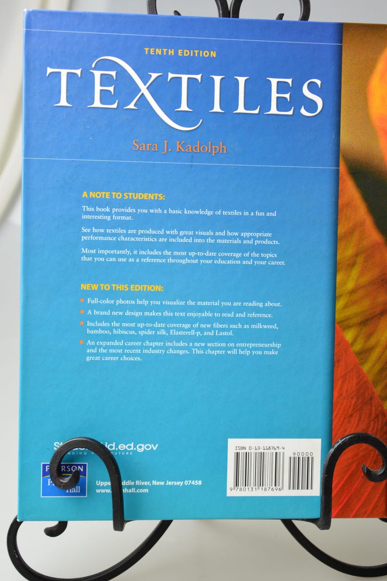 Puede incluir: La contraportada de un libro azul titulado "TEXTILES" de Sara J. Kadolph. El libro es la d&eacute;cima edici&oacute;n e incluye fotos a todo color, un nuevo dise&ntilde;o y una cobertura actualizada de nuevas fibras. El libro tambi&eacute;n incluye un cap&iacute;tulo de carrera ampliado con una nueva secci&oacute;n sobre emprendimiento.