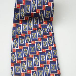 May include: A necktie featuring a repeating geometric pattern of dark blue rectangles and gold diamond shapes. Each diamond contains a small blue floral motif, and the design is accented with small red squares interspersed between the shapes.