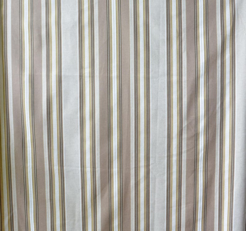 Puede incluir: Una tela con rayas verticales en tonos beige, blanco, marr&oacute;n y dorado. Las rayas son de diferentes anchos, creando una apariencia texturizada. La tela parece ser un material de peso ligero a medio.