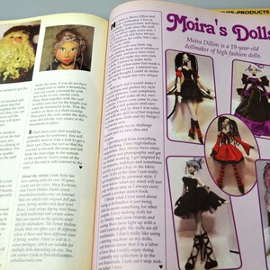 May include: A magazine spread featuring Moira's Dolls, a dollmaker of high fashion dolls. The spread showcases several dolls with different styles and outfits, including a black and white dress, a red and black dress, and a purple and black dress. The text "Moira's Dolls" is prominently displayed at the top of the page.
