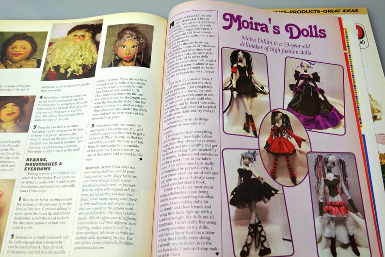 May include: A magazine spread featuring Moira's Dolls, a dollmaker of high fashion dolls. The spread showcases several dolls with different styles and outfits, including a black and white dress, a red and black dress, and a purple and black dress. The text "Moira's Dolls" is prominently displayed at the top of the page.