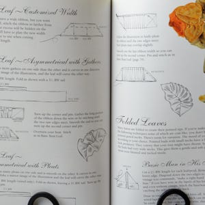 Peut inclure: Un livre avec des instructions sur la fa&ccedil;on de faire des fleurs en ruban. Le livre comprend des diagrammes et des illustrations de diff&eacute;rents types de feuilles, y compris des feuilles en forme de bateau, des feuilles pli&eacute;es et un homme de base dans son kimono. Le livre comprend &eacute;galement une photo d'une fleur en ruban finie.