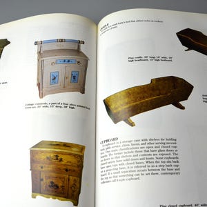 K&ouml;nnte beinhalten: Ein Buch, das auf einer Seite verschiedene antike M&ouml;belst&uuml;cke zeigt, darunter einen bemalten Holztisch, einen bemalten Holzschrank, einen bemalten Holzschrank, eine Kiefernholzwiege und einen Kiefernholzkasten. Der Text auf der Seite beschreibt die M&ouml;belst&uuml;cke und ihre Abmessungen.