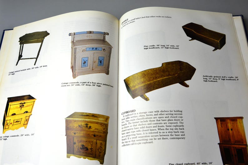 K&ouml;nnte beinhalten: Ein Buch, das auf einer Seite verschiedene antike M&ouml;belst&uuml;cke zeigt, darunter einen bemalten Holztisch, einen bemalten Holzschrank, einen bemalten Holzschrank, eine Kiefernholzwiege und einen Kiefernholzkasten. Der Text auf der Seite beschreibt die M&ouml;belst&uuml;cke und ihre Abmessungen.