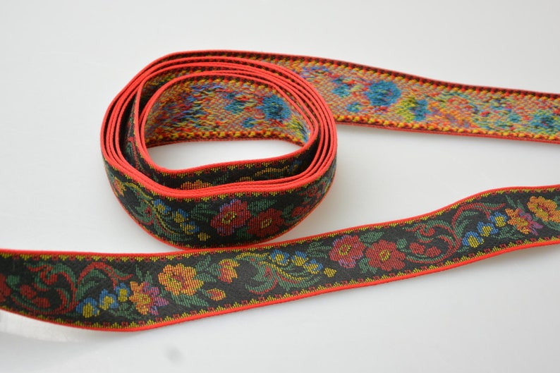 May include: A black and red ribbon with a floral pattern. The ribbon is woven with colorful threads and has a red border.