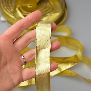 May include: A roll of gold metallic ribbon with a satin finish. The ribbon is approximately 2.5 cm wide and has a subtle shimmer.