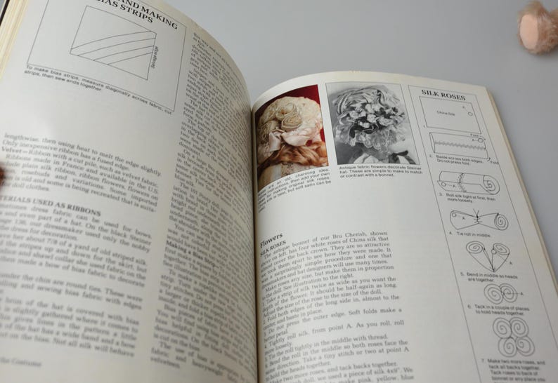 Pode incluir: Um livro vintage aberto em uma p&aacute;gina sobre como fazer rosetas de seda. A p&aacute;gina inclui instru&ccedil;&otilde;es e diagramas sobre como fazer as rosetas. O livro tamb&eacute;m tem uma se&ccedil;&atilde;o sobre como fazer flores de seda.
