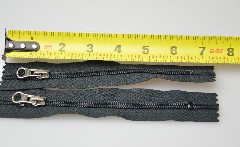 May include: Two black zipper pulls with silver sliders, measured against a yellow tape measure. The tape measure reads 20.3 cm.