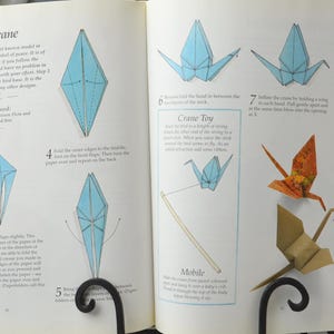 May include: A book with instructions on how to fold origami cranes. The book shows different steps for folding the paper into a crane shape. The book also includes instructions for making a crane toy, a mobile, and a peace crane.