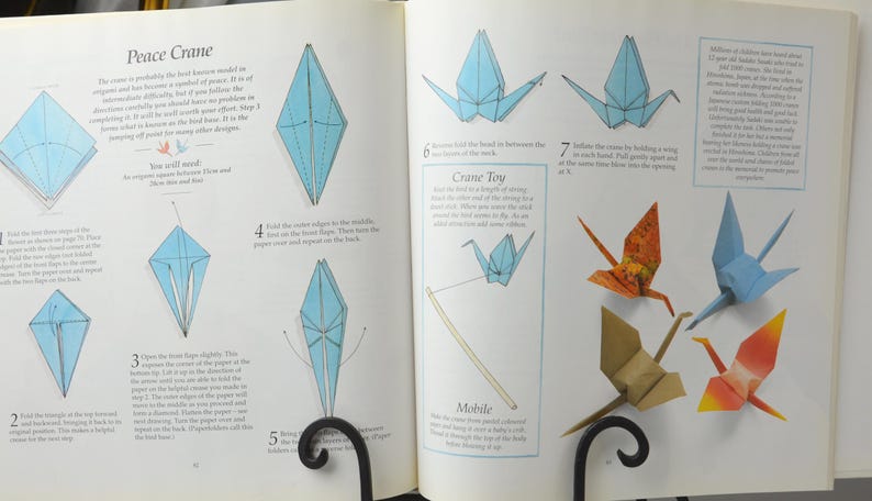 May include: A book with instructions on how to fold origami cranes. The book shows different steps for folding the paper into a crane shape. The book also includes instructions for making a crane toy, a mobile, and a peace crane.