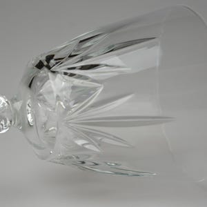 May include: A clear crystal wine glass with a long stem and a wide bowl. The glass features intricate starburst patterns cut into the bowl, reflecting light. The stem is also detailed, adding to the elegant design. Ideal for serving wine.