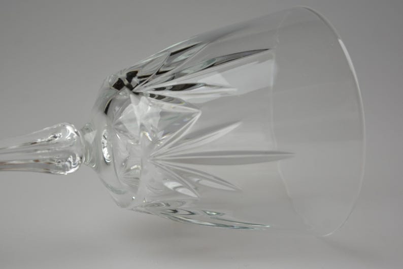 May include: A clear crystal wine glass with a long stem and a wide bowl. The glass features intricate starburst patterns cut into the bowl, reflecting light. The stem is also detailed, adding to the elegant design. Ideal for serving wine.
