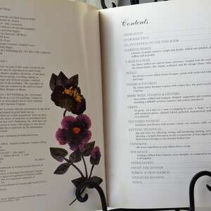 Peut inclure: Un livre intitul&eacute; "Candied Flowers" avec une image rapproch&eacute;e d'une fleur violette et noire en tissu. La couverture du livre pr&eacute;sente une table des mati&egrave;res avec des sujets tels que "Introduction", "P&eacute;tales", "Boutons de baies, &eacute;tamines et centres", "Vert", "Finitions textur&eacute;es", "Techniques d'obtention", "Crinoline", "La danse", "Appr&eacute;ciation", "&Agrave; propos de l'auteur", "Sources de rubans et de garnitures", "Lectures sugg&eacute;r&eacute;es" et "Index".