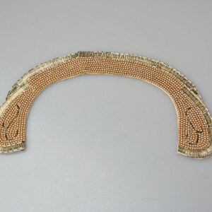 May include: A gold-colored beaded collar with a scalloped edge. The beads are arranged in a pattern that creates a decorative design.