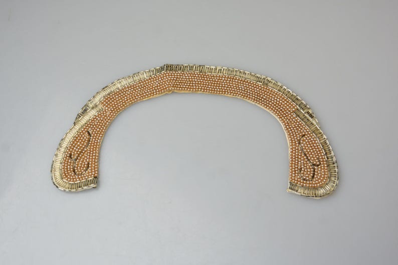 May include: A gold-colored beaded collar with a scalloped edge. The beads are arranged in a pattern that creates a decorative design.
