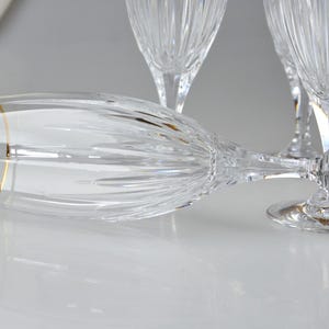 Pu&ograve; includere: Un set di fl&ucirc;te da champagne in cristallo trasparente con motivi tagliati verticali e un sottile bordo dorato sul bordo superiore. Un fl&ucirc;te &egrave; posizionato orizzontalmente in primo piano, mentre altri due sono in piedi sullo sfondo.