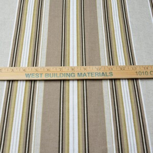 Puede incluir: Tela con rayas verticales en beige, blanco, verde oliva y negro. Una regla de madera con el texto "WEST BUILDING MATERIALS" y "1010 CHESTNUT ST" cruza la tela. La tela es adecuada para decoraci&oacute;n del hogar o ropa.