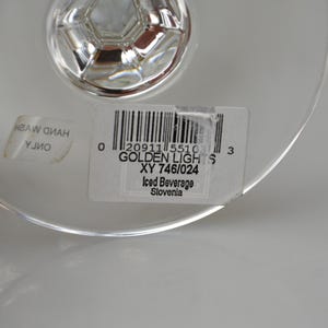 Pu&ograve; includere: Primo piano di un bicchiere trasparente con stelo. Un'etichetta sul bicchiere recita "GOLDEN LIGHTS" e "Iced Beverage". Il bicchiere ha una base decorativa ed &egrave; probabilmente per servire bevande.