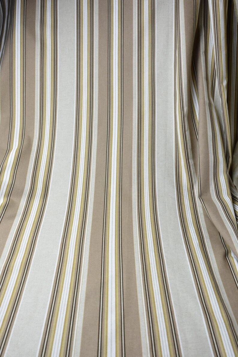 Puede incluir: Tela con rayas verticales en tonos beige, blanco y verde oliva. Las rayas var&iacute;an en ancho, creando una apariencia texturizada. La tela est&aacute; drapeada, lo que sugiere que podr&iacute;a usarse para cortinas o tapicer&iacute;a.