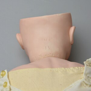May include: The back of a porcelain doll head with the inscription "Germany 13 K.M. Watson" on the back of the neck.
