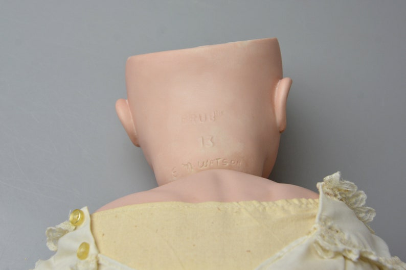 May include: The back of a porcelain doll head with the inscription "Germany 13 K.M. Watson" on the back of the neck.