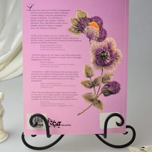 Peut inclure: Une couverture de livre rose avec un motif floral mettant en sc&egrave;ne une fleur de ruban violette, rose et orange. Le titre du livre est "Beauties in Bloom" et l'auteur est Candace Kling. La couverture du livre comprend &eacute;galement des citations d'autres auteurs et designers.