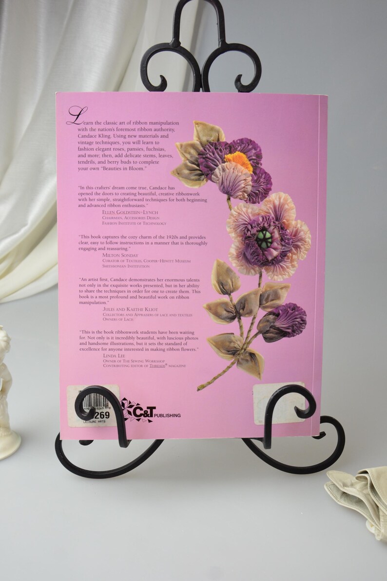 Peut inclure: Une couverture de livre rose avec un motif floral mettant en sc&egrave;ne une fleur de ruban violette, rose et orange. Le titre du livre est "Beauties in Bloom" et l'auteur est Candace Kling. La couverture du livre comprend &eacute;galement des citations d'autres auteurs et designers.