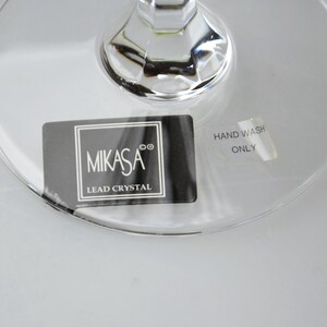 Pu&ograve; includere: Una base in cristallo al piombo trasparente con un adesivo rettangolare nero che riporta il testo bianco MIKASA e LEAD CRYSTAL. Un adesivo argentato pi&ugrave; piccolo riporta il testo HAND WASH ONLY. Il vetro presenta un attacco dello stelo sfaccettato.