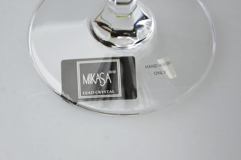 Pu&ograve; includere: Una base in cristallo al piombo trasparente con un adesivo rettangolare nero che riporta il testo bianco MIKASA e LEAD CRYSTAL. Un adesivo argentato pi&ugrave; piccolo riporta il testo HAND WASH ONLY. Il vetro presenta un attacco dello stelo sfaccettato.