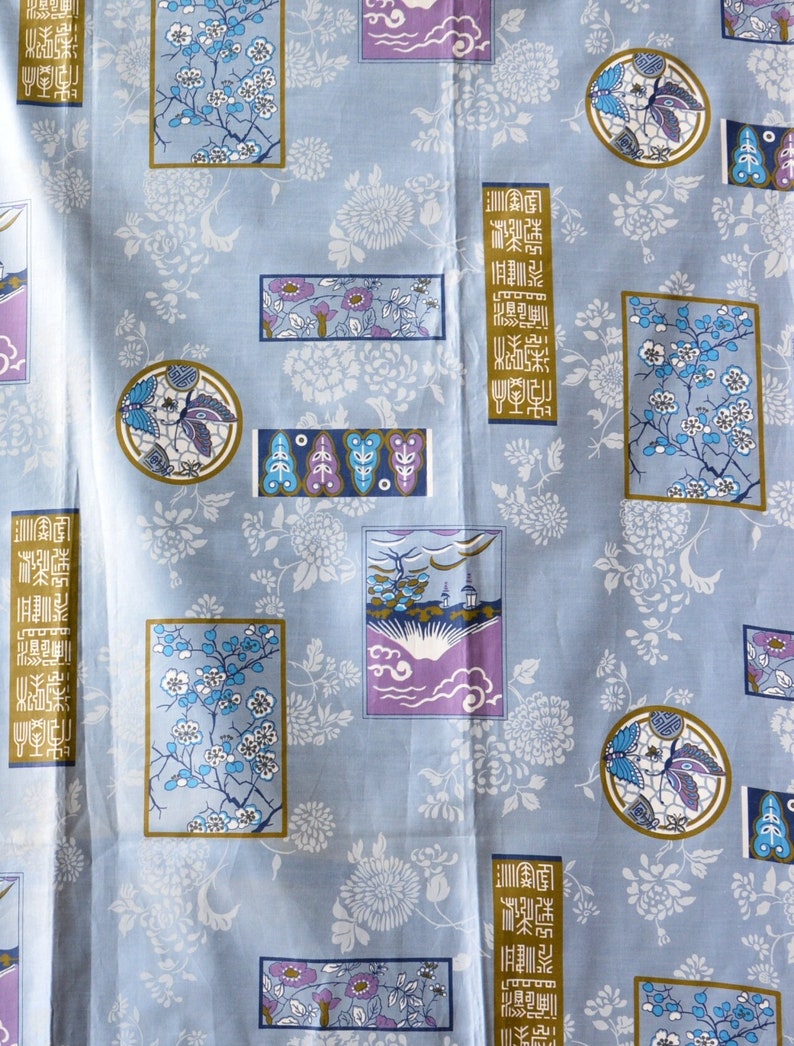 May include: A blue fabric with a repeating pattern of white flowers, butterflies, and Japanese characters. The characters are in a gold rectangle and read "金魚", which means goldfish.