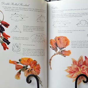 Peut inclure: Un livre ouvert sur deux pages montrant des instructions pour la fabrication de fleurs en tissu. La page de gauche montre un bouton de rose &agrave; double roul&eacute; avec un sch&eacute;ma des &eacute;tapes. La page de droite montre une fleur &agrave; double roul&eacute; avec un sch&eacute;ma des &eacute;tapes. Le texte sur les pages indique "Double Rolled Rosebud" et "Double"