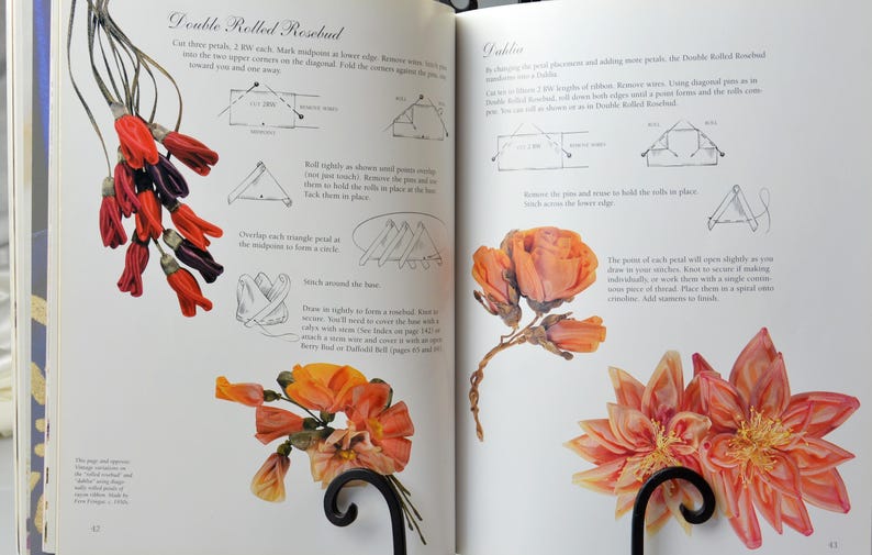 Peut inclure: Un livre ouvert sur deux pages montrant des instructions pour la fabrication de fleurs en tissu. La page de gauche montre un bouton de rose &agrave; double roul&eacute; avec un sch&eacute;ma des &eacute;tapes. La page de droite montre une fleur &agrave; double roul&eacute; avec un sch&eacute;ma des &eacute;tapes. Le texte sur les pages indique "Double Rolled Rosebud" et "Double"