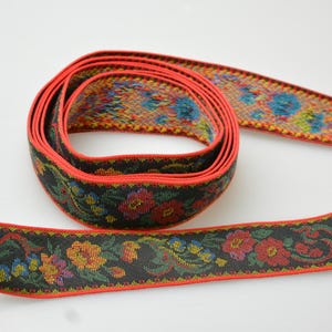 May include: Black and red woven ribbon with a floral pattern. The ribbon has a red border and a black background with colorful flowers and leaves.