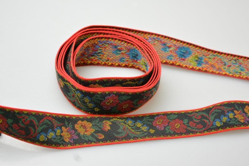 May include: Black and red woven ribbon with a floral pattern. The ribbon has a red border and a black background with colorful flowers and leaves.
