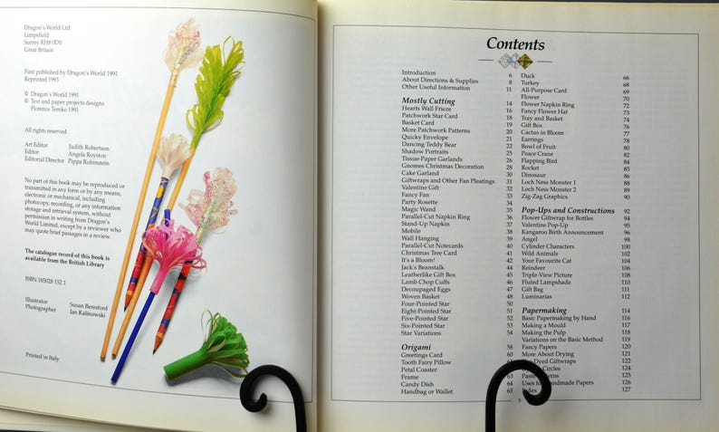 May include: A book titled "Papercraft" with a table of contents listing various paper crafts, including origami, pop-ups, and papermaking techniques. The book cover features colorful paper flowers and a bookmarker.