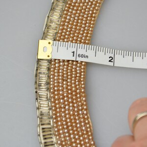 May include: A close-up of a pearl necklace with a gold-toned metal clasp. The necklace is being measured with a tape measure, showing it is 1 1/2 inches long.