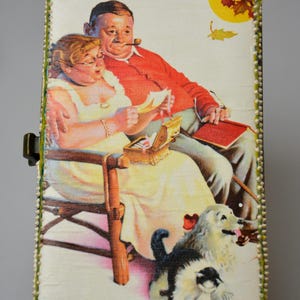 Op de afbeelding: Rechthoekige houten doos met een scharnierend deksel, met een vintage illustratie van een stel dat brieven leest, een kleine schatkist en twee honden. De doos is afgewerkt met groene en witte kralen.