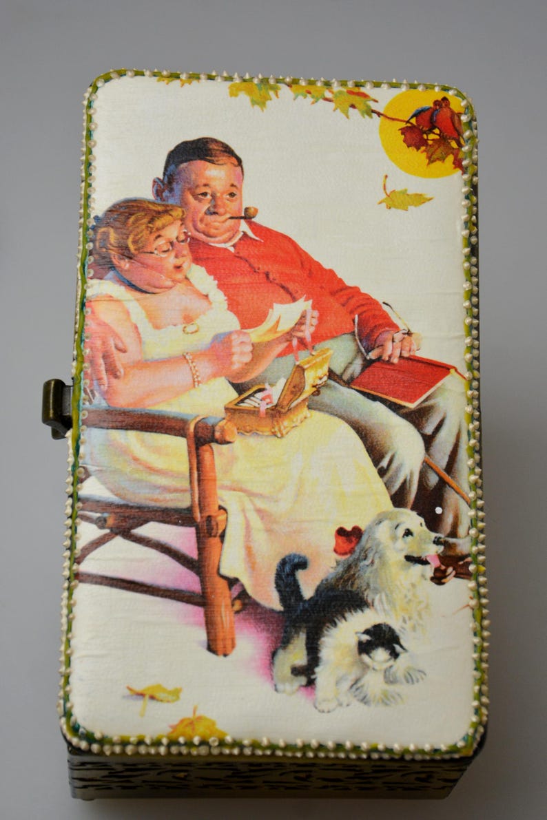 Op de afbeelding: Rechthoekige houten doos met een scharnierend deksel, met een vintage illustratie van een stel dat brieven leest, een kleine schatkist en twee honden. De doos is afgewerkt met groene en witte kralen.